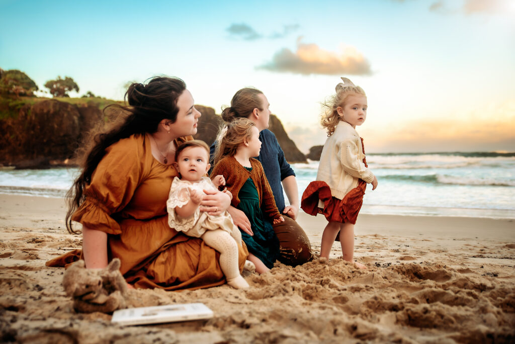 A family on the beach during a styled photography session, wearing coordinated outfits and enjoying playful, natural moments together - Paula Jane Photography